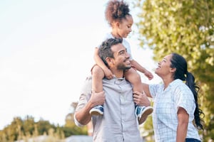 A family outdoors together with a young girl riding on the father's shoulders